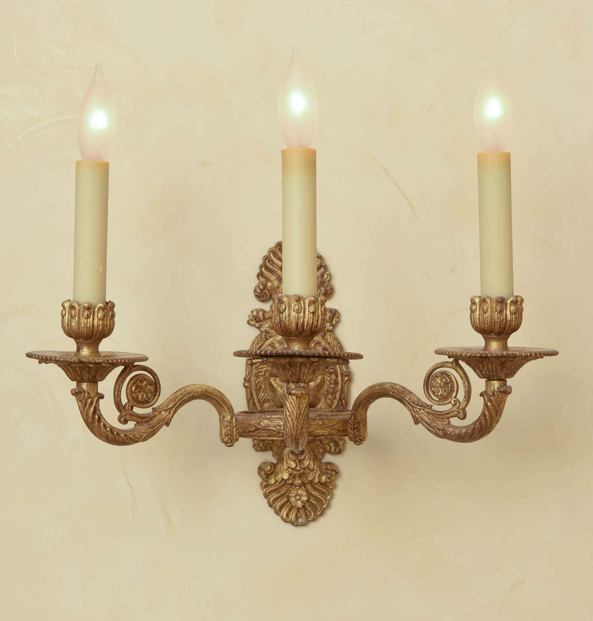 Each backplate centered by a lion mask set between stylized acanthus leaf ornament; issuing three outward scrolling, foliate candle arms; electrified.