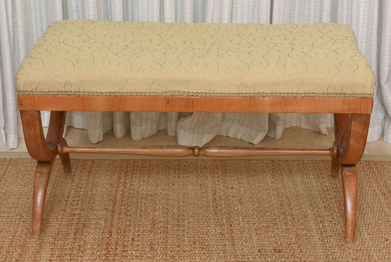 The upholstered rectangular seat over the seat rail and X-form side supports headed by gilt-metal rosettes and joined by a stretcher.