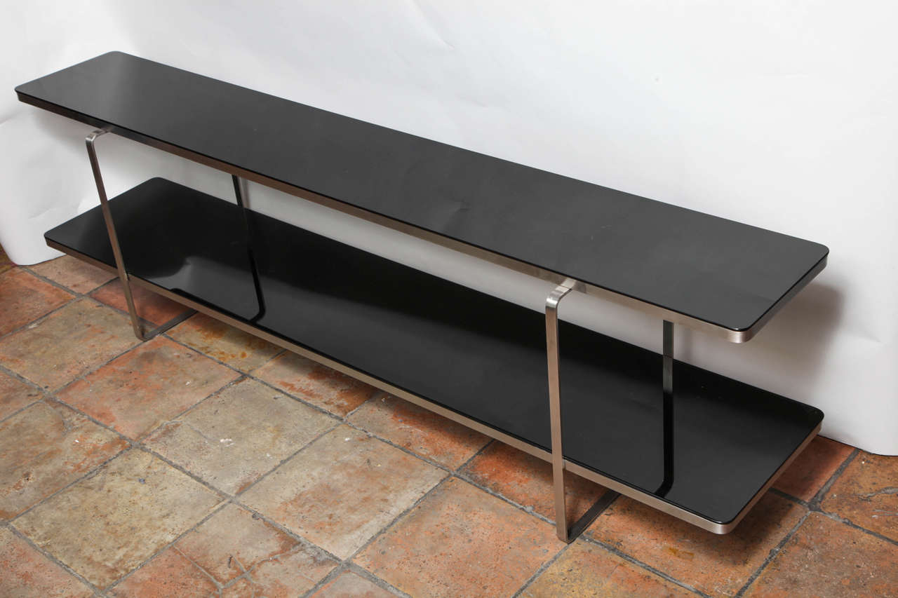 A wonderful two-tiered brushed steel console table with two long black glass shelves.