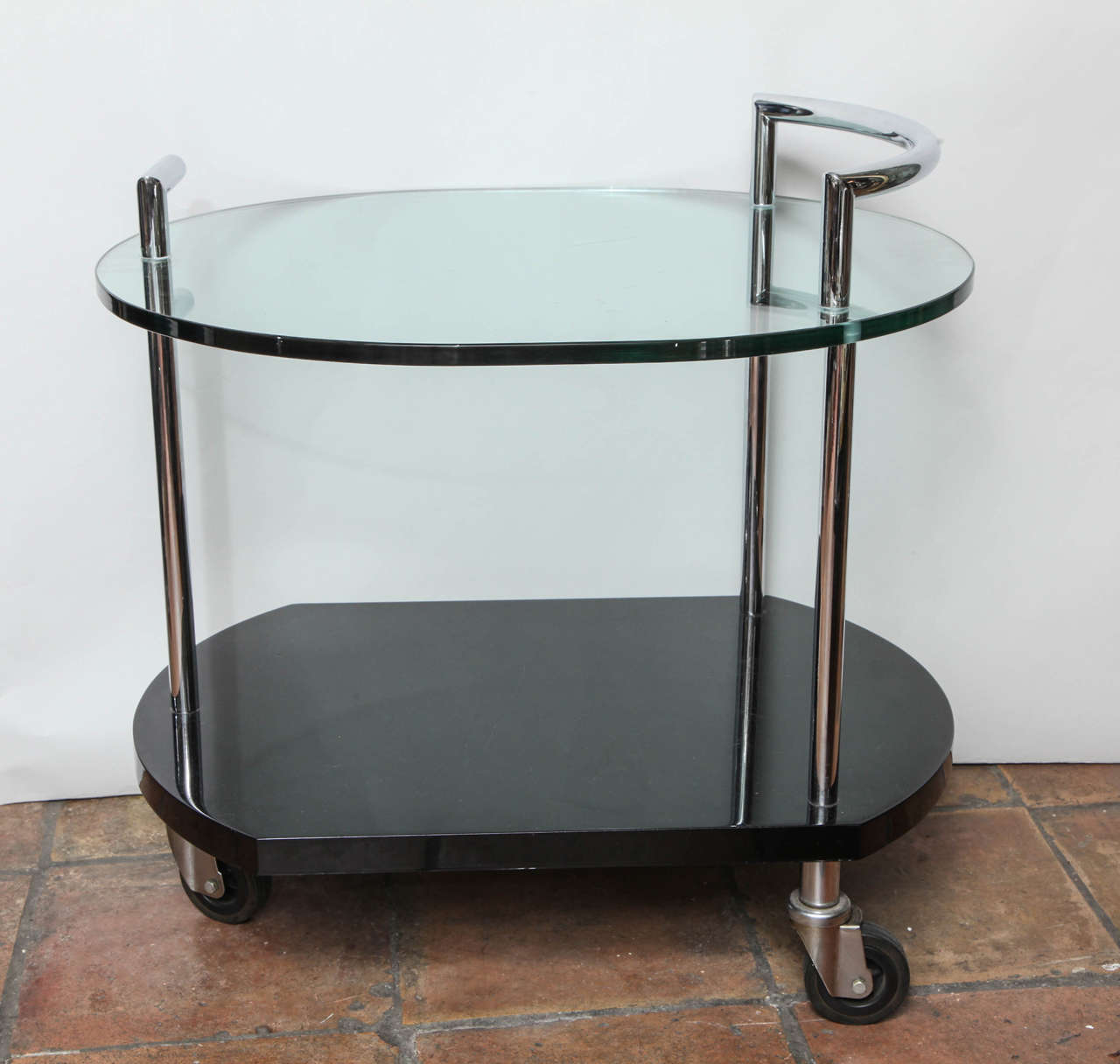 A charming and practical two-tiered modernist bar cart with nickel-plated handles over a glass shelf and a lower lacquered shelf over swivel casters.