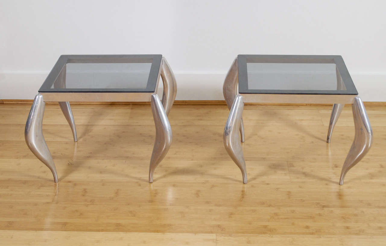 A pair of chrome and glass side tables with curvaceous, tapered legs.
