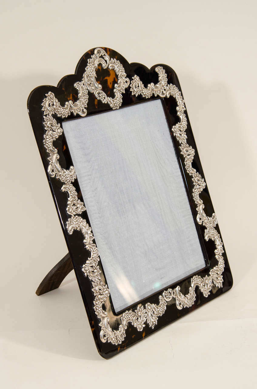 This large ornate faux tortoiseshell frame has intricate floral and foliate sterling silver-mounted design with scalloped top and original wood easel back.