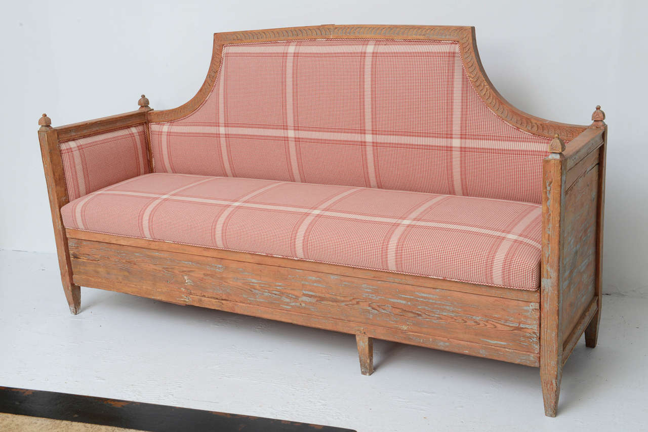Swedish wooden bench or sofa with pull-out bed, recently upholstered in a red and white checked cotton. The bench has an original stain and remnants of the original paint that wore off over the years. The bottom pulls out and the bench turns into a