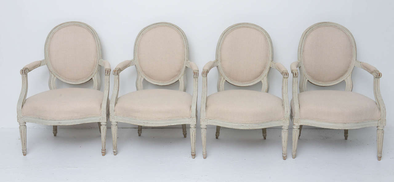 Set of four Swedish Gustavian style armchairs from 1770s with a medallion back, gray washed wooden frame with seat, back and elbow rests upholstered in a wheat color linen.