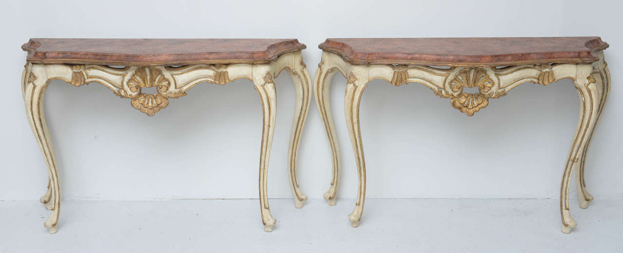 Pair of Italian Florentine Consoles in Luois XV style, legs and base are in a cream color and gilt. The middle of the apron is ornamented with a Rococo shell.  Faux Painted Marble Wood Top. Please contact us for individual purchase.