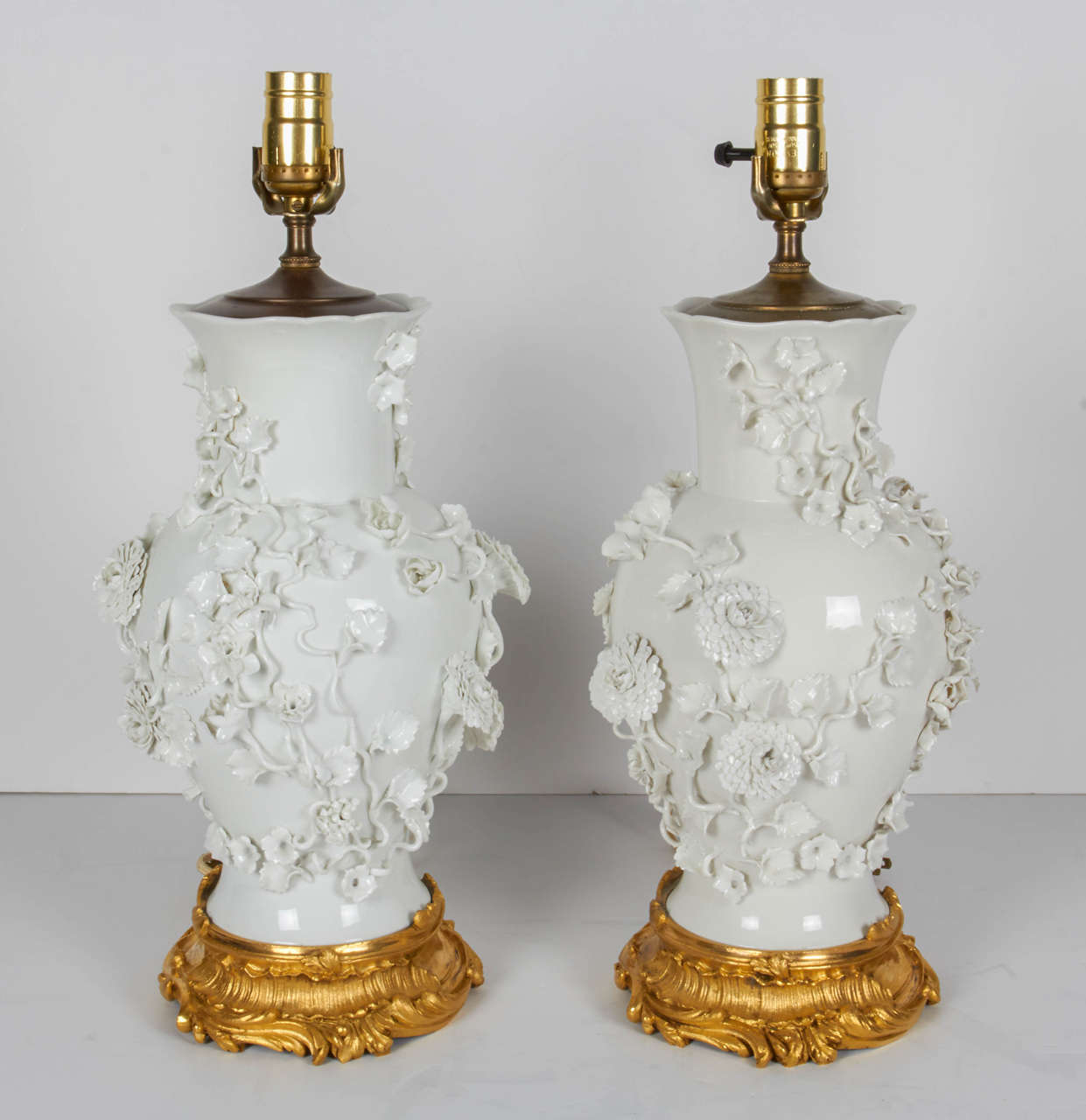 An unusual pair of antique Blanc de Chine porcelain vases mounted as lamps with Louis XV style richly carved ormolu bases. Each baluster shaped vase is embellished in relief with porcelain flowers and leaves, circa mid-1800s. Later, converted to
