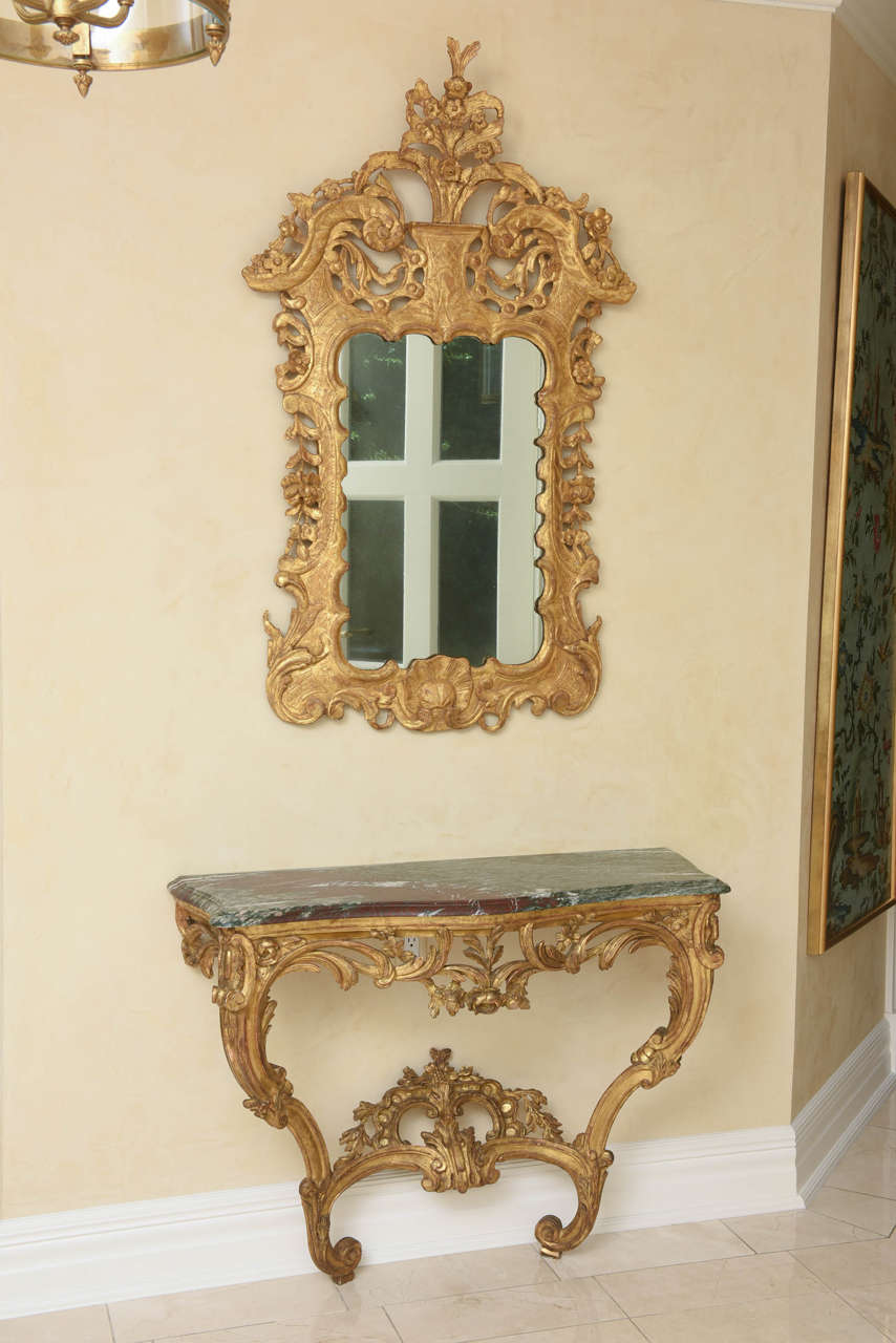 Each with serpentine-form rosso antico marble top over a rose garland-festooned frieze and foliate-carved scrolling volutes joined by a C-scroll stretcher carved with a cabochon-enriched clasp.