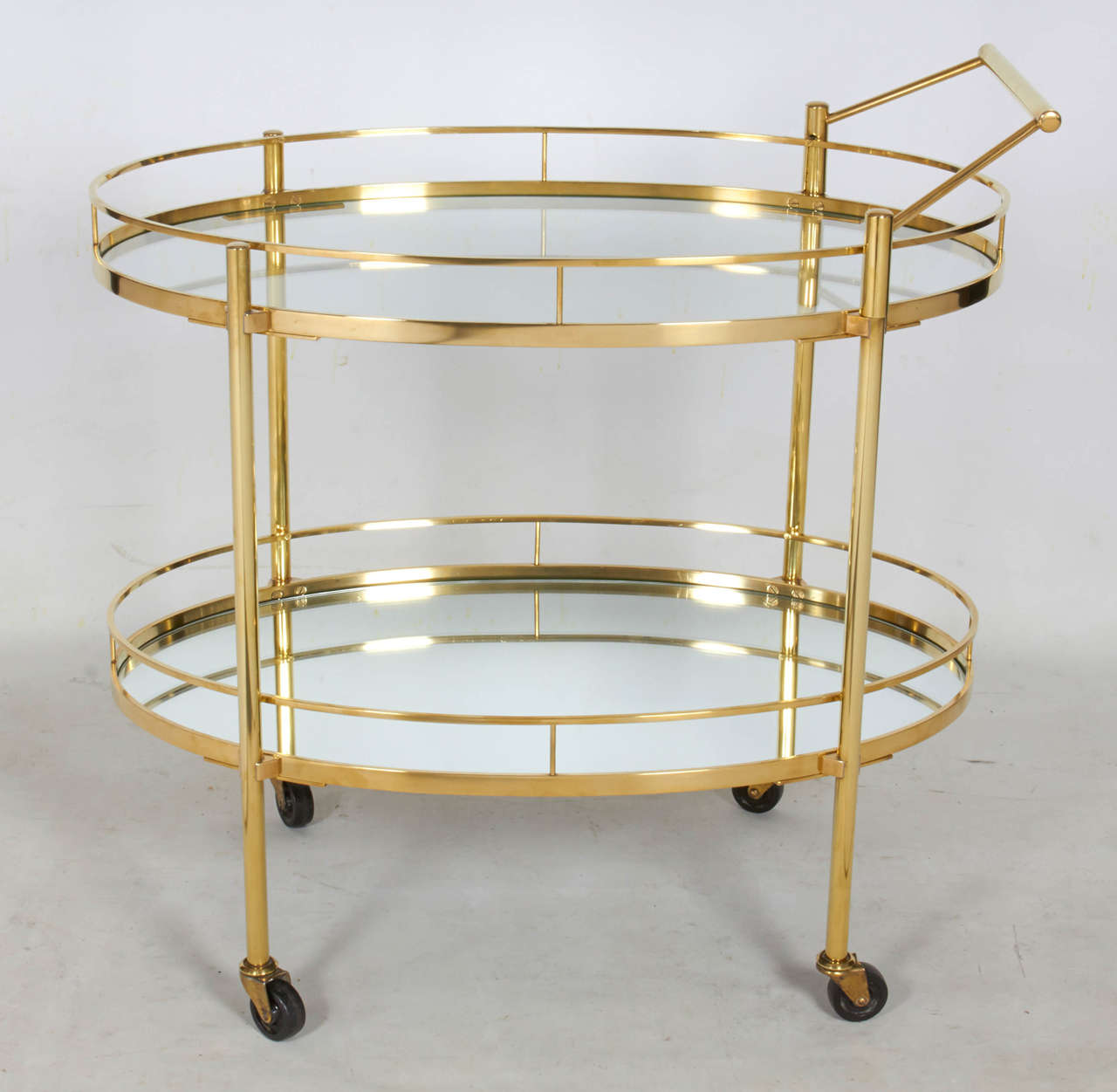 Chic serving or bar cart in gleaming polished brass. The cart has a graceful oval form and is very nicely detailed with a glass top shelf and a mirrored lower shelf. The handle is adjustable and easily pulls off if desired. Please contact for