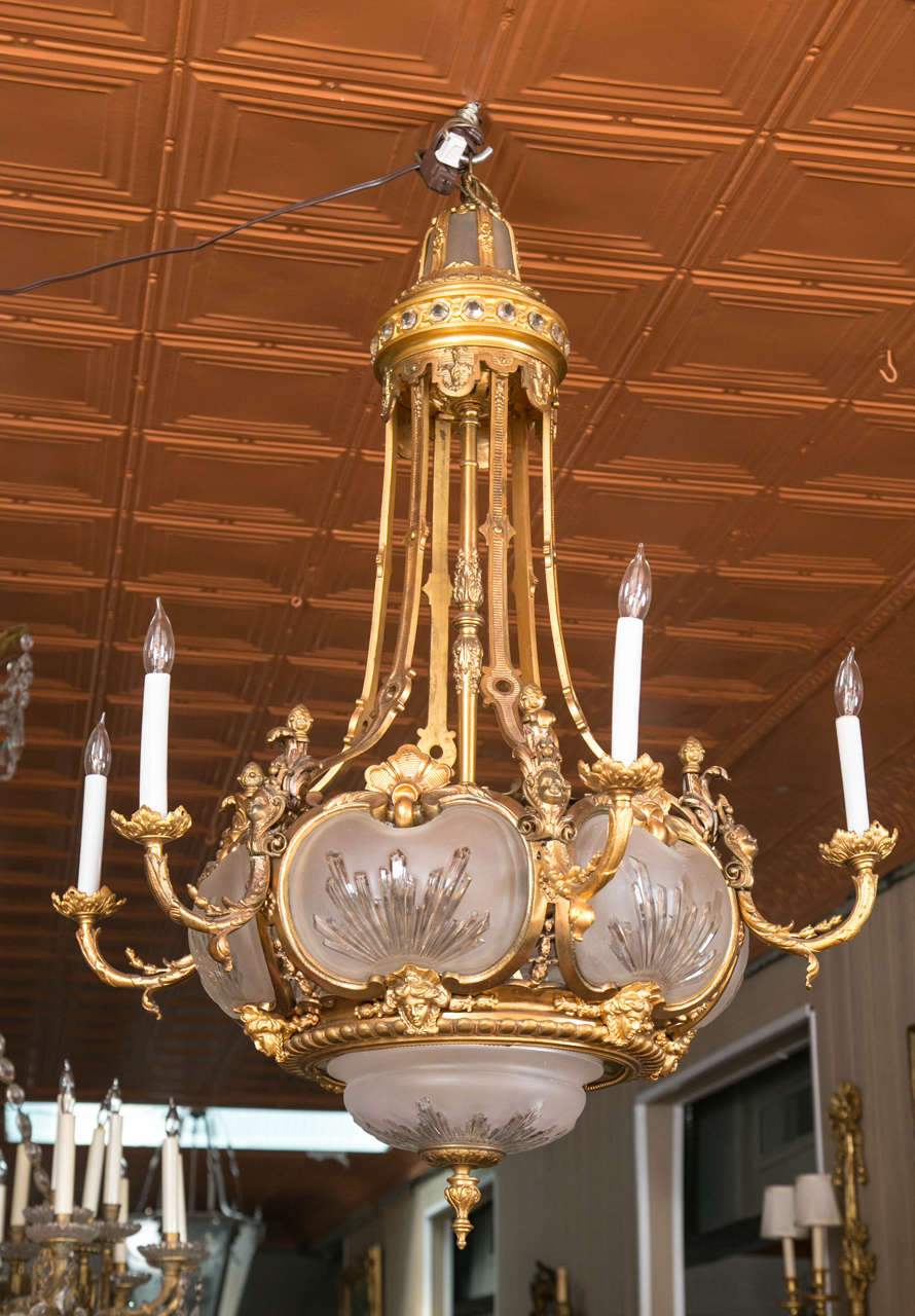 A beautiful and unusual Louis XVI style bronze chandelier. It features cut frosted glass inserts which have lights inside and a single light at the top. The chandelier has six outside arms that light up and three interior lights at it's center. The