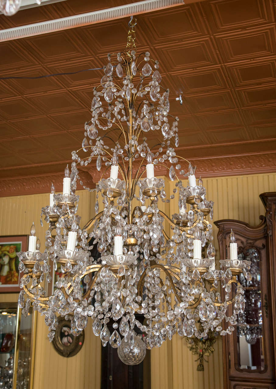 This wonderful Italian gilt metal chandelier features twenty lights and a dramatic tapered Christmas tree like shape. The crystals appear as a Cascade of raindrops from the top. It is elegant from top to bottom, where it is finished with a beautiful