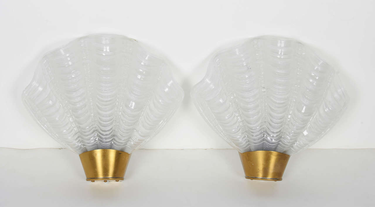 Art Deco sconces with elegant shell design. The sconces are comprised of white hand molded frosted glass with fluted details and stylized ridges created in the form of sea shells. The sconces feature petite brushed brass metal fittings and frames.