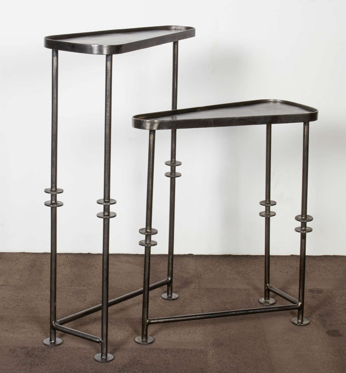 Pair of modernist Industrial side tables designed to nest in a variety of configurations. The tables feature a tripod leg design with welded metal disc details. The tables also feature asymmetrical crossbars along the base as well as triangular