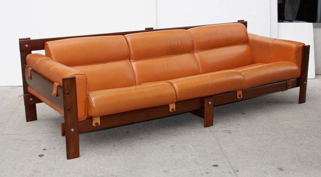 Modernist sofa with streamline form comprised of Brazilian rosewood frame with original cognac colored leather upholstery. The sofa has a linear block style frame design with sculpted back and seat cushions featuring sleek center seams. The