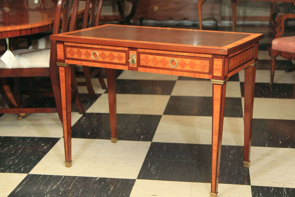 This early 20th century inlaid bureau plat features an attractive inlaid kingwood harlequin pattern along the front, sides and back. The brass-mounted mahogany legs are each inlaid with a kingwood band on their two out-facing sides. In a cohesive