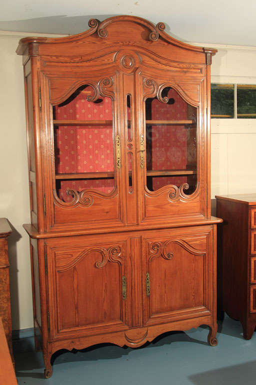 This French, stained pine buffet a deux corps with glass doors features deeply carved scrollwork on the crown, doors and feet. Nicely rounded corners, shaped panel doors and recessed panel sides combine to complete the elegant appearance of this