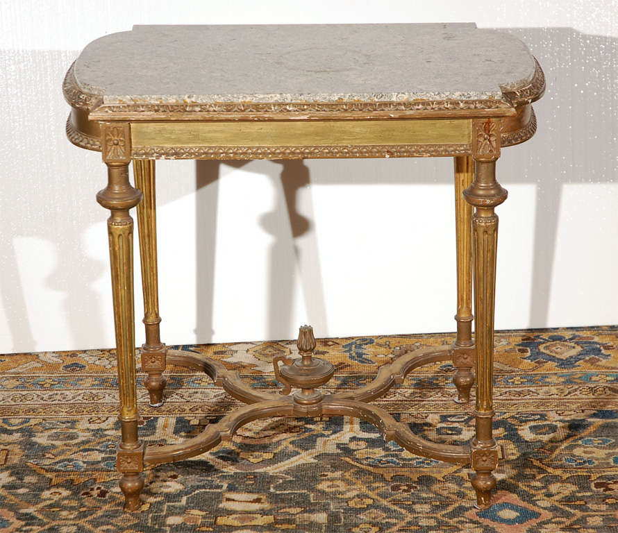 Hand carved, bench made hardwood French table with gilded finish.   Fluted legs, serpentine crossed stretcher with urn and flame detail. Original marble top.