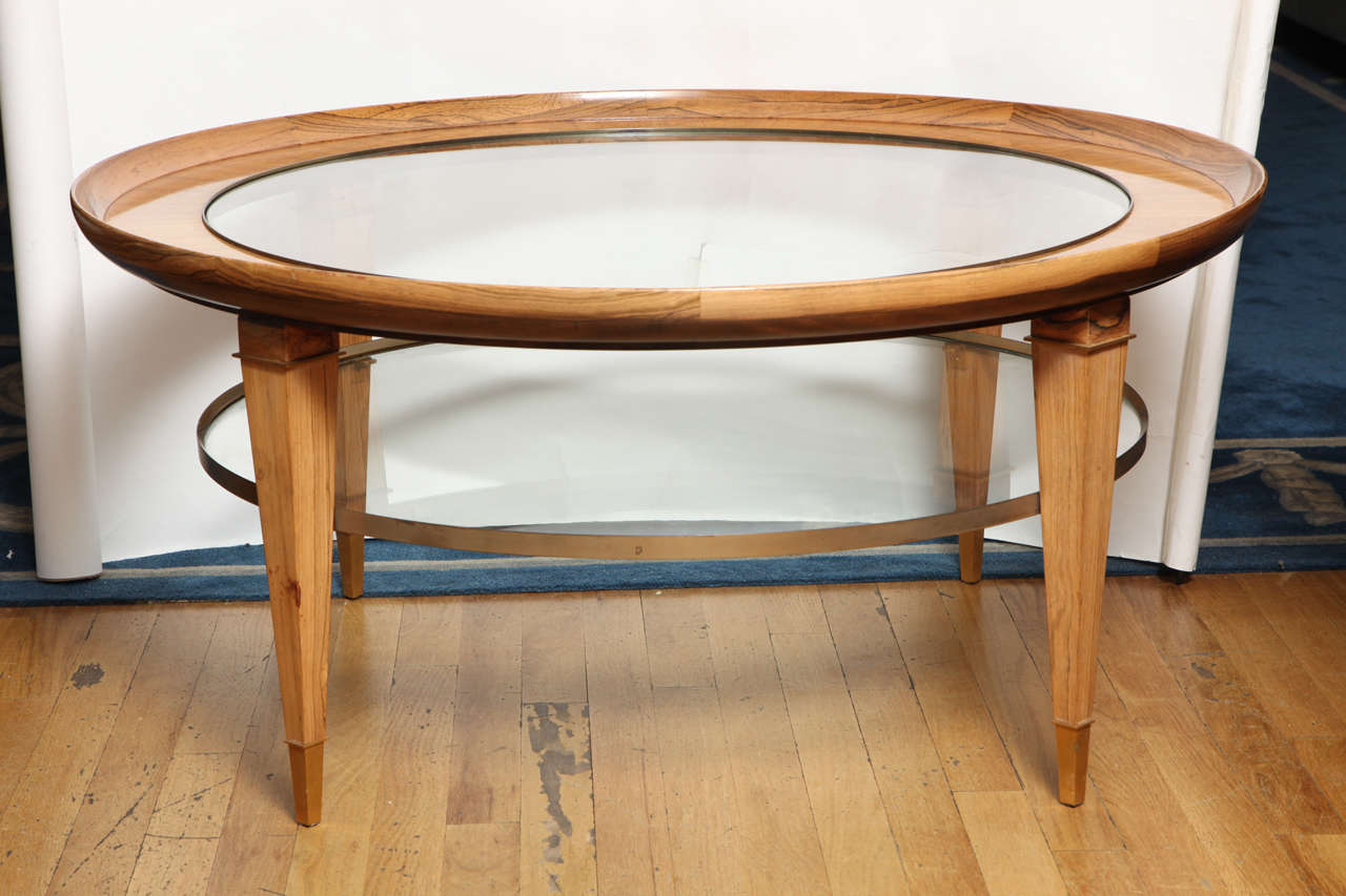 A round, custom-made two-tiered rosewood coffee table, the veneered upper tier with upswept edge and inset glass top, the square tapering legs having gold brushed finish metal sabots and supporting metal frame with inset glass.