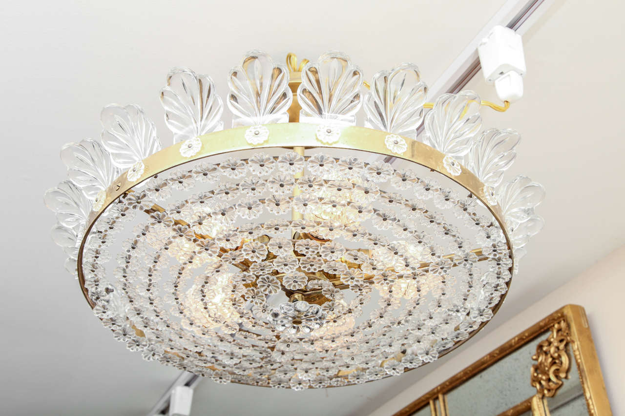 A French Bagues style flush-mounted ceiling fixture, the bronze frame encircled by rosettes and issuing molded glass feather-shaped ornaments, the three electric light sockets concealed by a frame completely covered by small glass rosettes.