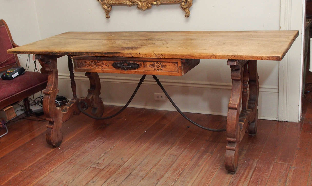 A late 19 century trestle table, the top of wide boards and over a drawer, the drawer with a handsome, hand forged pull.  The trestle sides with a nice turned rail and connected by a pair of scrolling iron supports.  Nice and tall, with ample leg