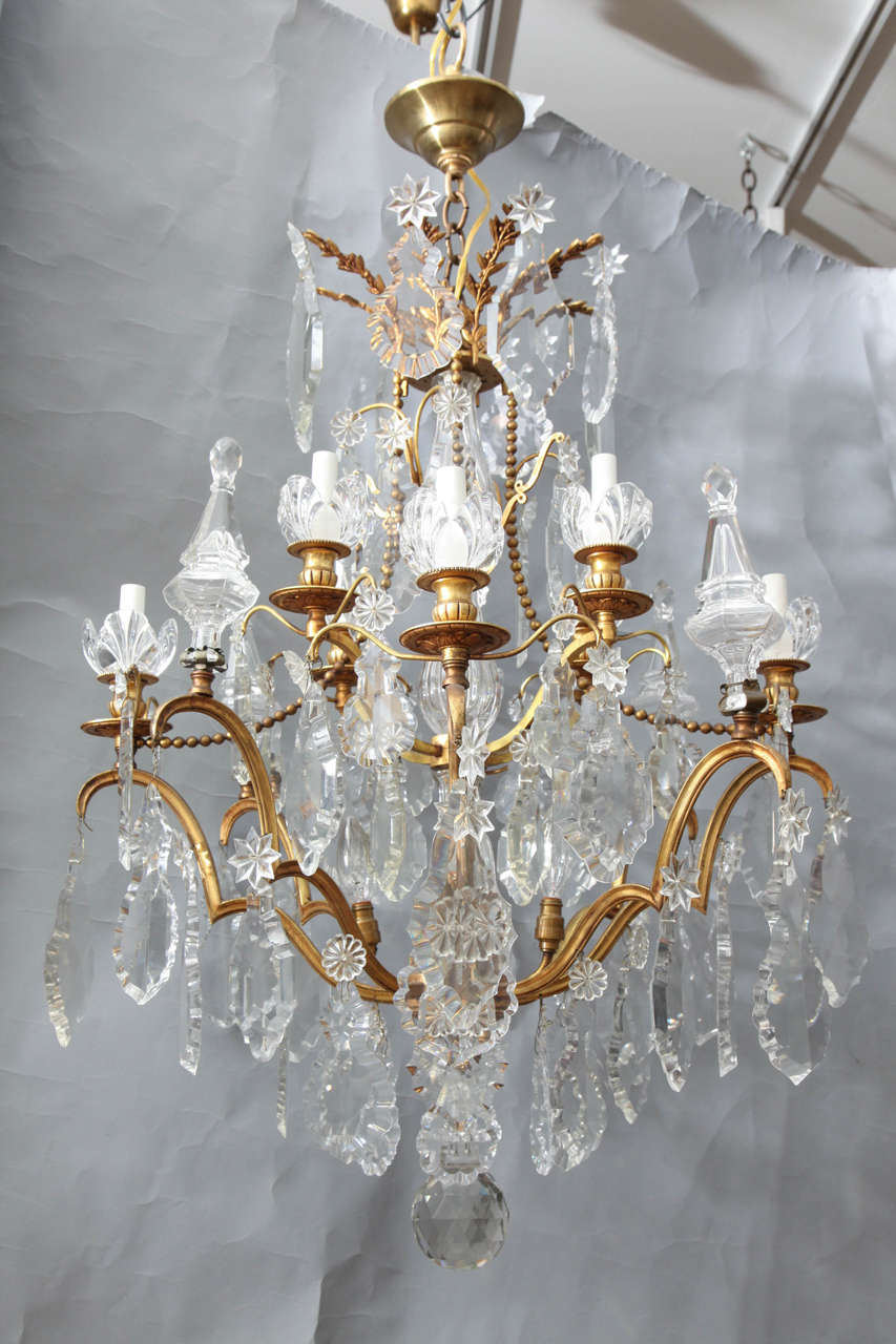 An 8 light French Louis XVI-style gilt bronze chandelier with two tiers of cut crystal rose-shaped bobeches. The frame draped with cut crystal drops and obelisk-shaped finials. The chandelier frame having four additional sockets illuminating