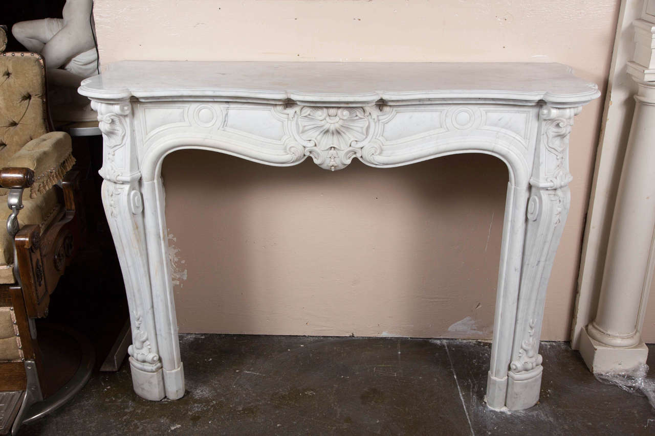 This is a decorative carved marble mantel with decorative legs and a much embellished carved center. The marble is white with light veining. This can be seen at our 1800 South Grand Ave, Los Angeles store.