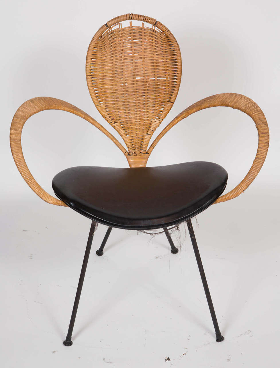 This is a black four legged metal chair with large over exaggerated wicker arms and a teardrop shaped wicker back. The seat is a black vinyl round edge cushion base. This can be seen at our 1800 South Grand Ave location in downtown LA.
