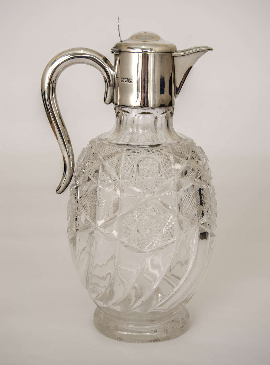 An impressive Edwardian silver mounted claret jug, of oval form with a plain silver mount with hinged lid. The excellent crystal glass has a plain fluted design at the base rising to a delightfully embellished upper body. Measures: Height 10 inches