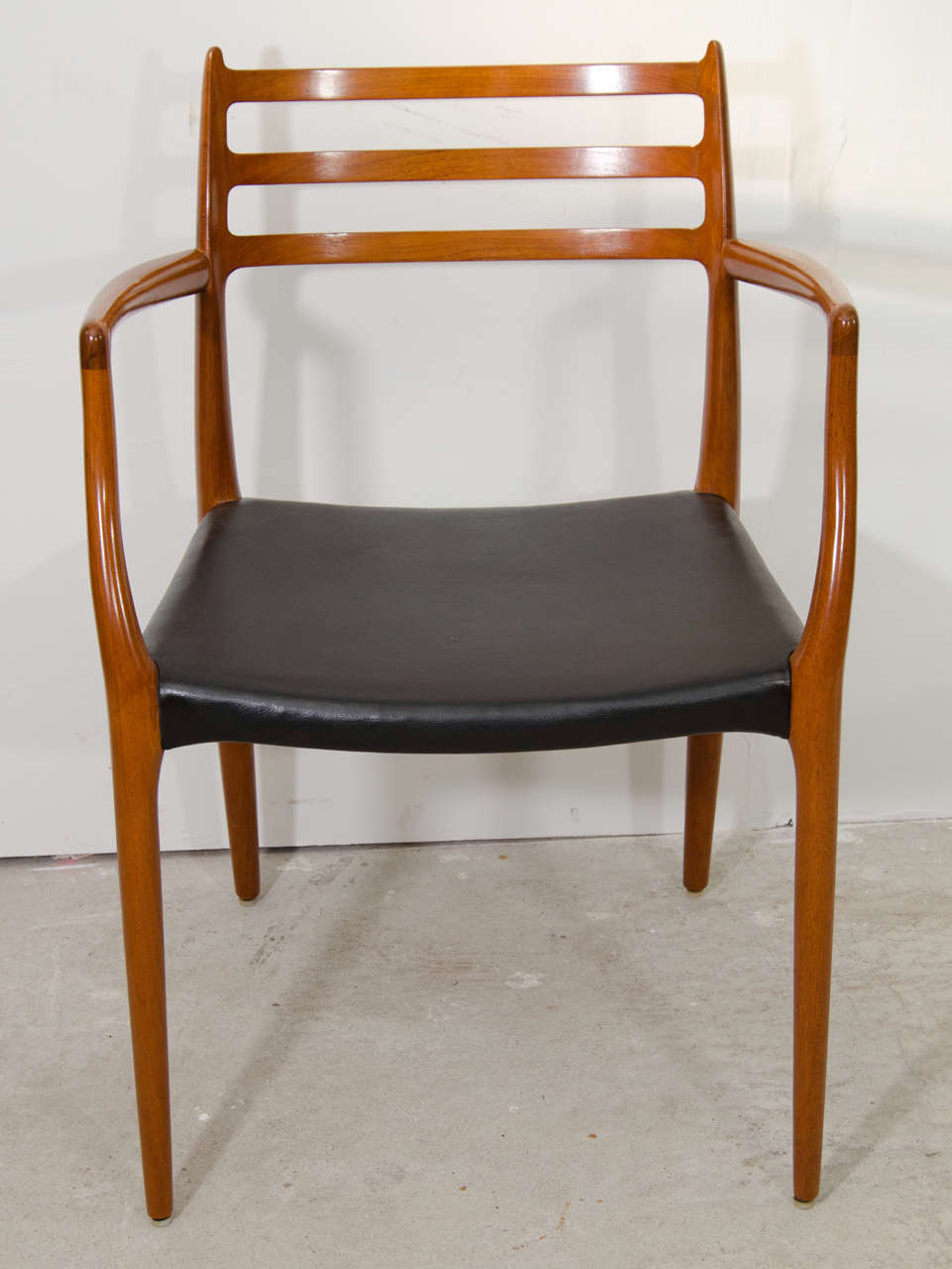 A mid century pair of teak wood dining chairs with arms in original black vinyl designed by Niels Otto Moller.