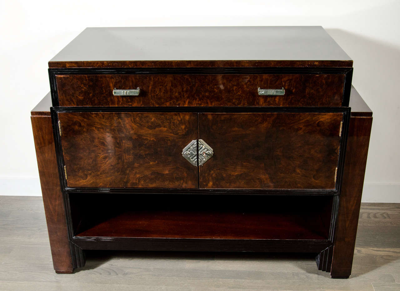 This stunning Art Deco skyscraper style cabinet/console features bookmatched burled walnut with black lacquer detailing and bronze fittings. The cabinet has a pair of center opening doors, a wide, deep drawer and an open shelf for storage. Fully