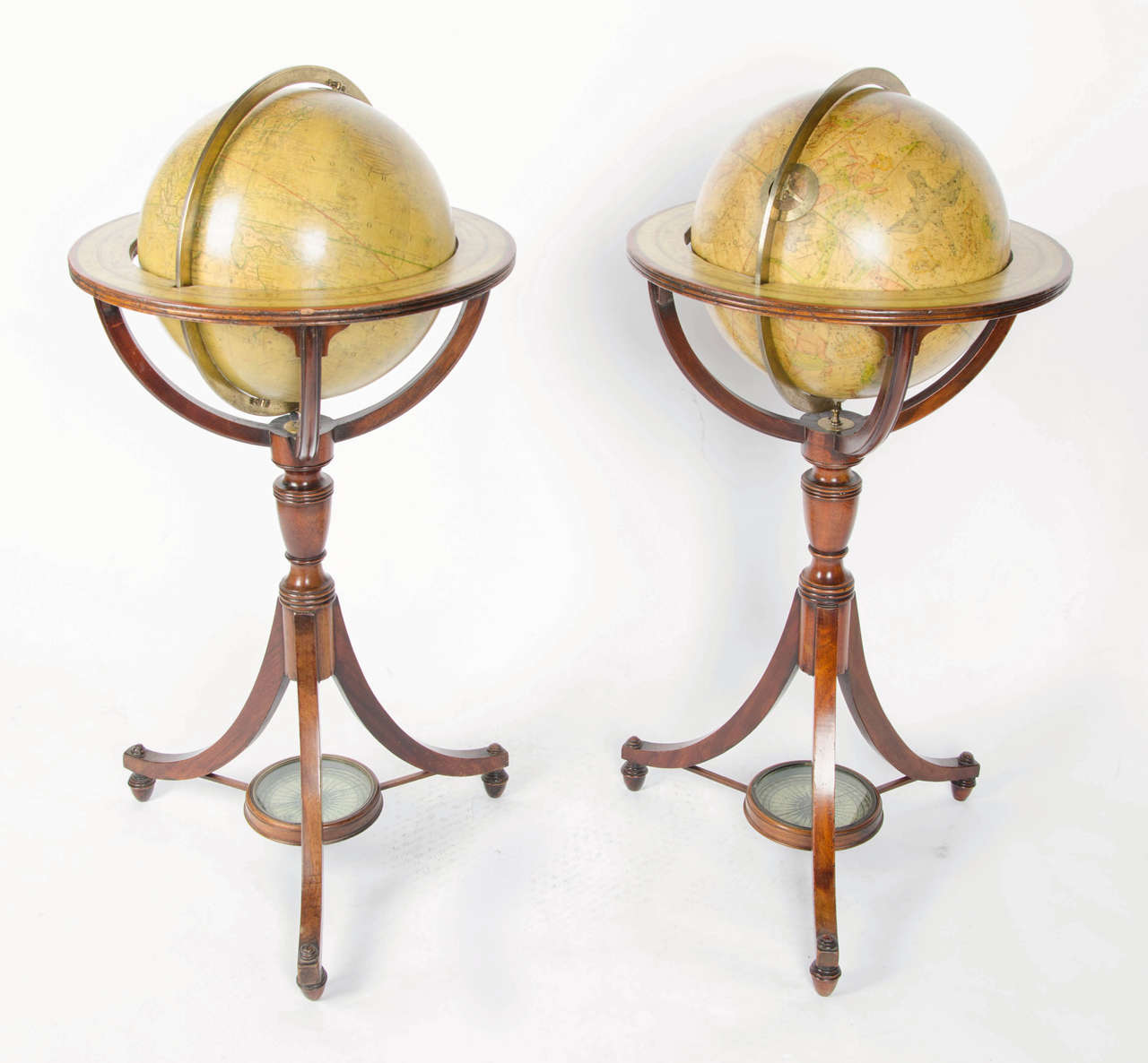 A pair of Regency terrestrial and celestial mahogany library globes with printed directionals and reeded standard on down swept curving tripod supports with compass stretcher, terminating in beehive formed feet.

Terrestrial globe with a maker's