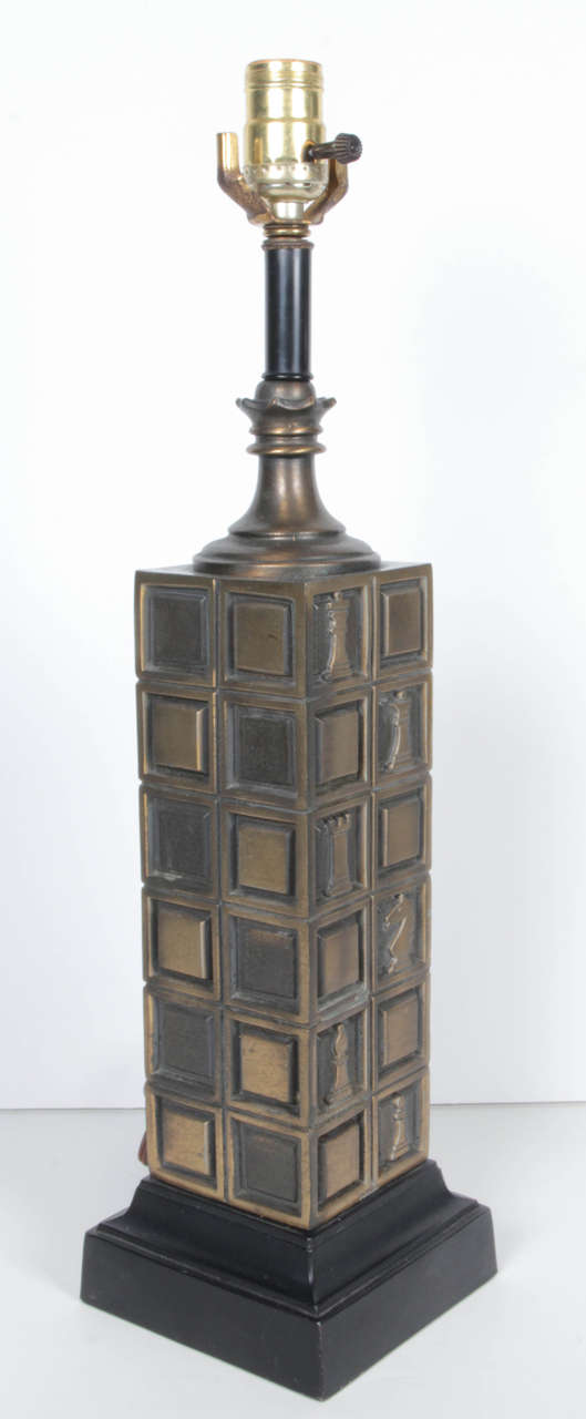 A pair of patinated brass lamps with a chess motif. The lamps sit on an ebonized wood base. Measurements are to top of socket.