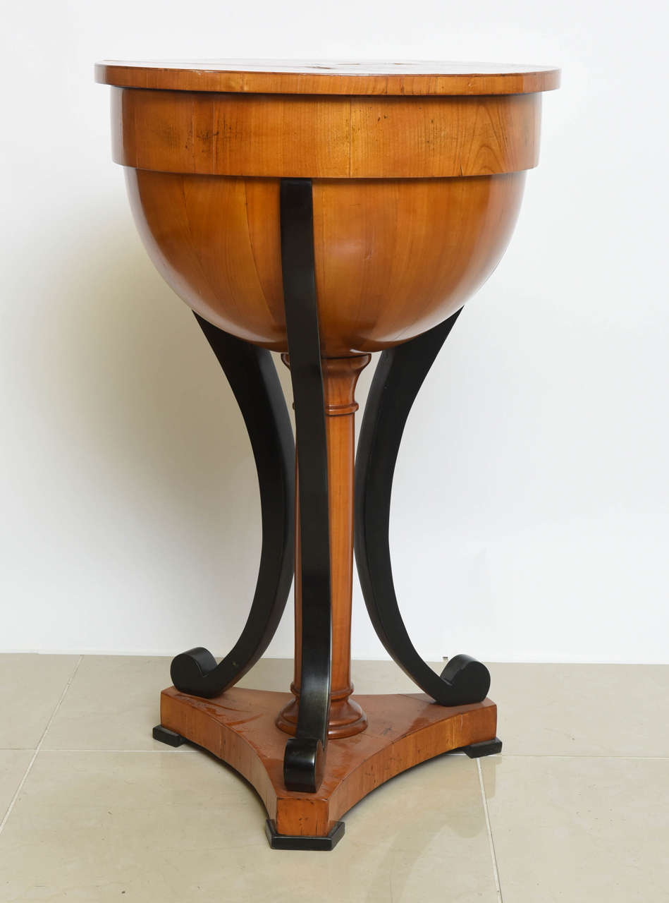 The round top with hinge to reveal a fitted interior, above a central column and scrolling legs on a tripartite plinth.