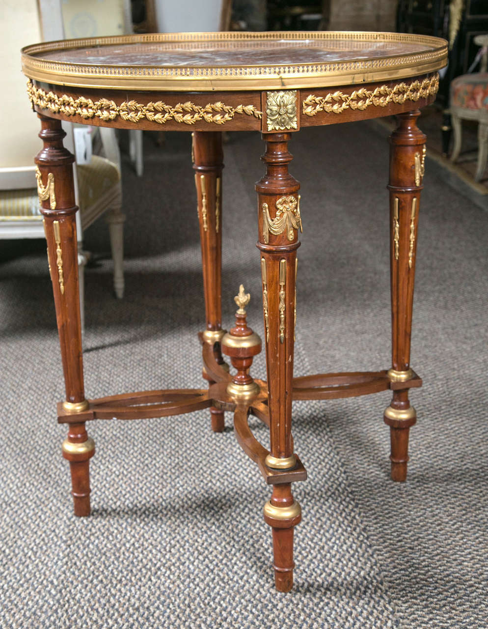 A beautiful French Louis XVI style mahogany end table or bouillotte table, circa 1920s, the circular rouse marble-top with a pierced bronze gallery frame, supported on a narrow frieze decorated with bronze mounts, raised on fluted legs joint by an