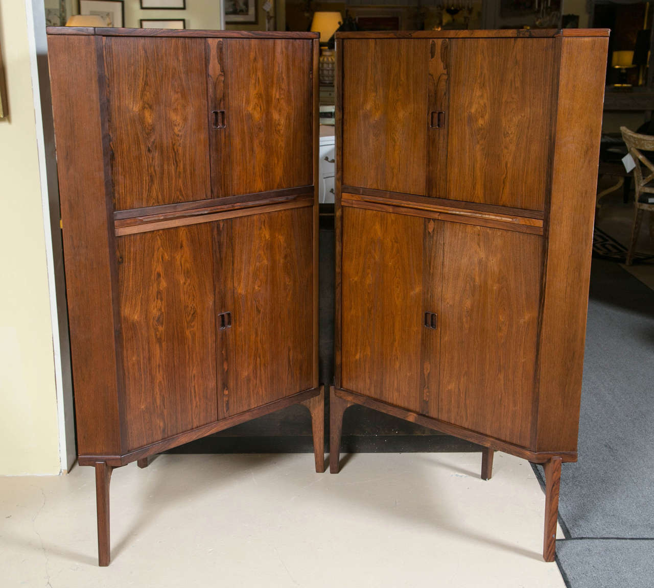 Pair of Mid-Century Modern Danish rosewood corner cabinets. Each having a conforming case fitted with adjustable shelves, a pull-out slide divides two sections, raised on tapering legs ending in pegged feet.