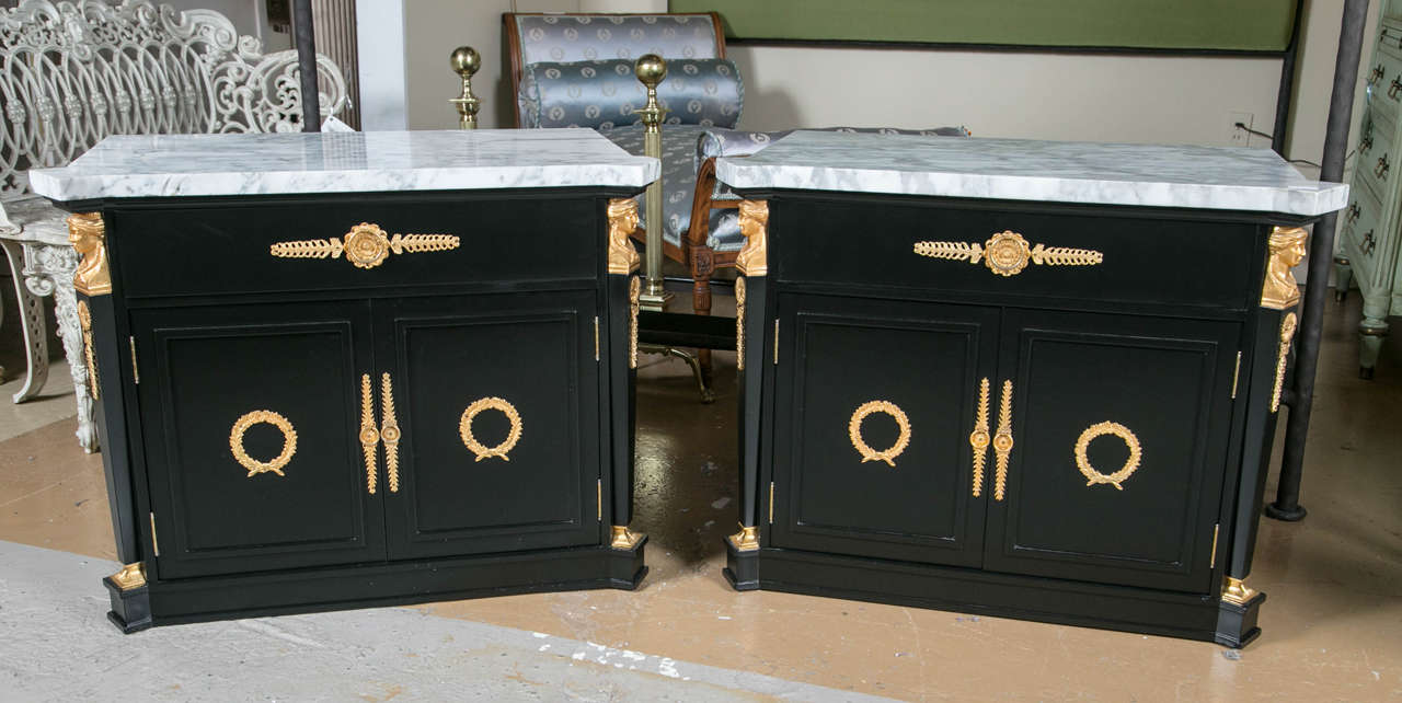 Pair of French Directoire style nightstands, circa 1950s, overall ebonized and decorated with bronze mounts, the white marble atop a conforming case fitted with a drawer over two cabinet doors, flanked by two columnar uprights headed by gilded