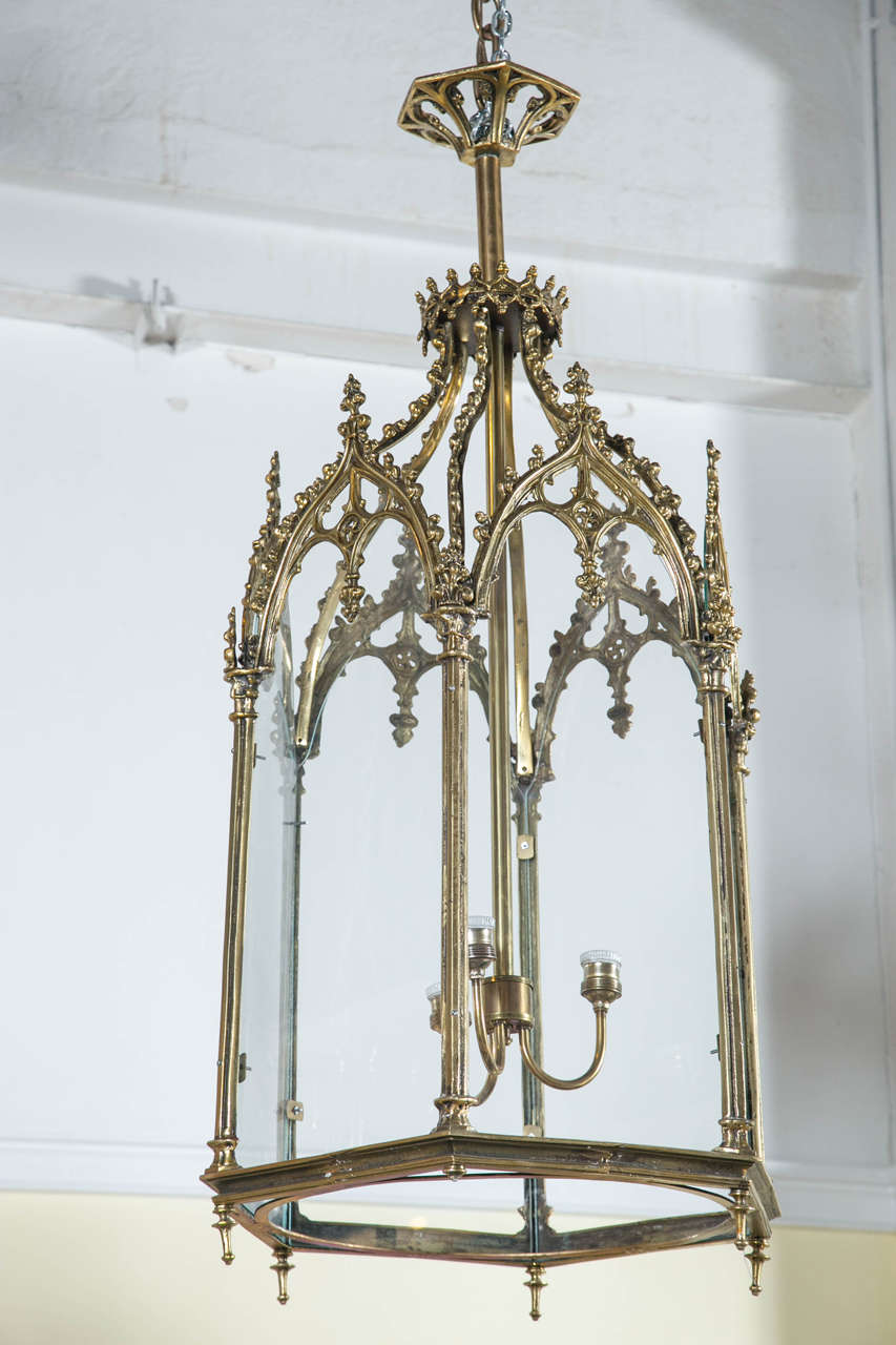 Pair of polygon bronze and glass antique lanterns. A fine pair of bronze lantern chandeliers. Each of the six-sided chandeliers with column form bronze sides terminating in carved pediments. Having four lights each recently wired. Both suspended by