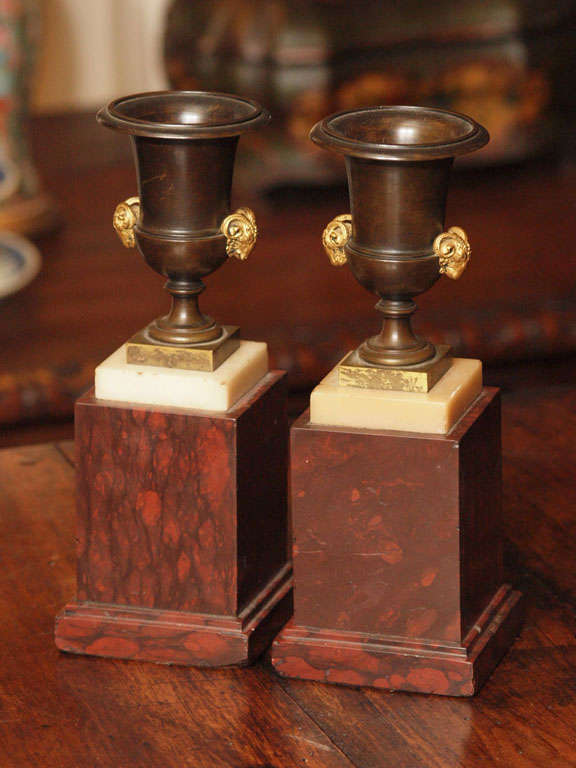 Pair of First Empire Patinated and gilt bronze campagna form urns with rams heads on rouge marble bases
