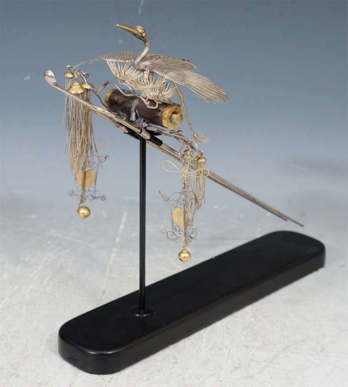 An antique Japanese hair ornament in silver with gilt detail. The piece depicts a crane, flowers and other hanging floral inspired details. The piece was made for the Oiran, the highest class of courtesan in the Edo period. It is mounted to a black