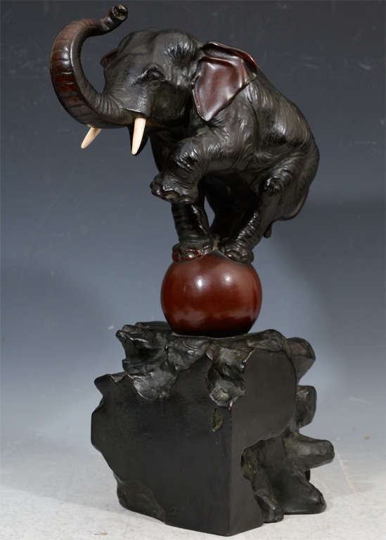 A vintage Japanese bronze sculpture of an elephant balancing on a red ball. The piece has fine detail in the elephant and dates from the Meiji period (1868-1912)