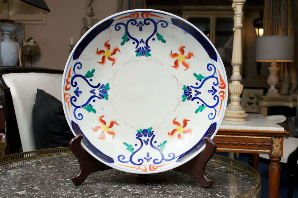 The large circular-shaped white ceramic glazed and hand-painted with red and yellow five-petaled flowers flanked by blue and green scroll designs.  In the manner of William Morris