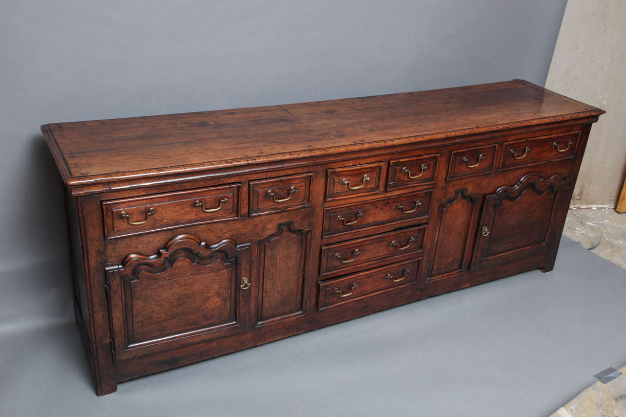 Queen Anne period English or Welsh low dresser of exceptional form and quality, the thumb molded top over ogee molded frieze over two wide and four narrow drawers, over scallop molded and raised paneled doors, flanking similarly shaped blind panels,