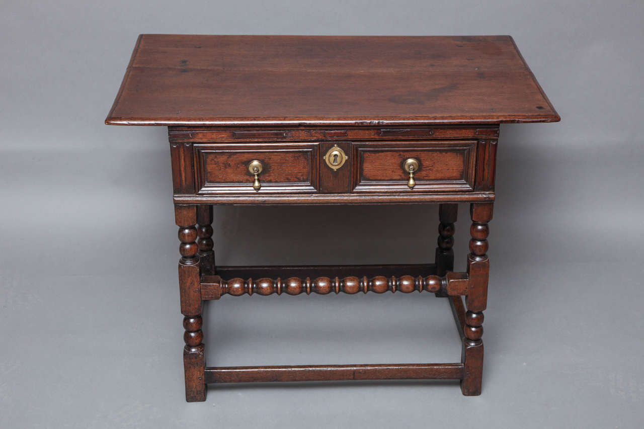 Good English 17th century oak side table, the two plank top having thumb molded edge, over single drawer with geometric panels surrounded by applied fruitwood bosses and cabochons, over heavy thumb molded support, standing on bobbin turned legs