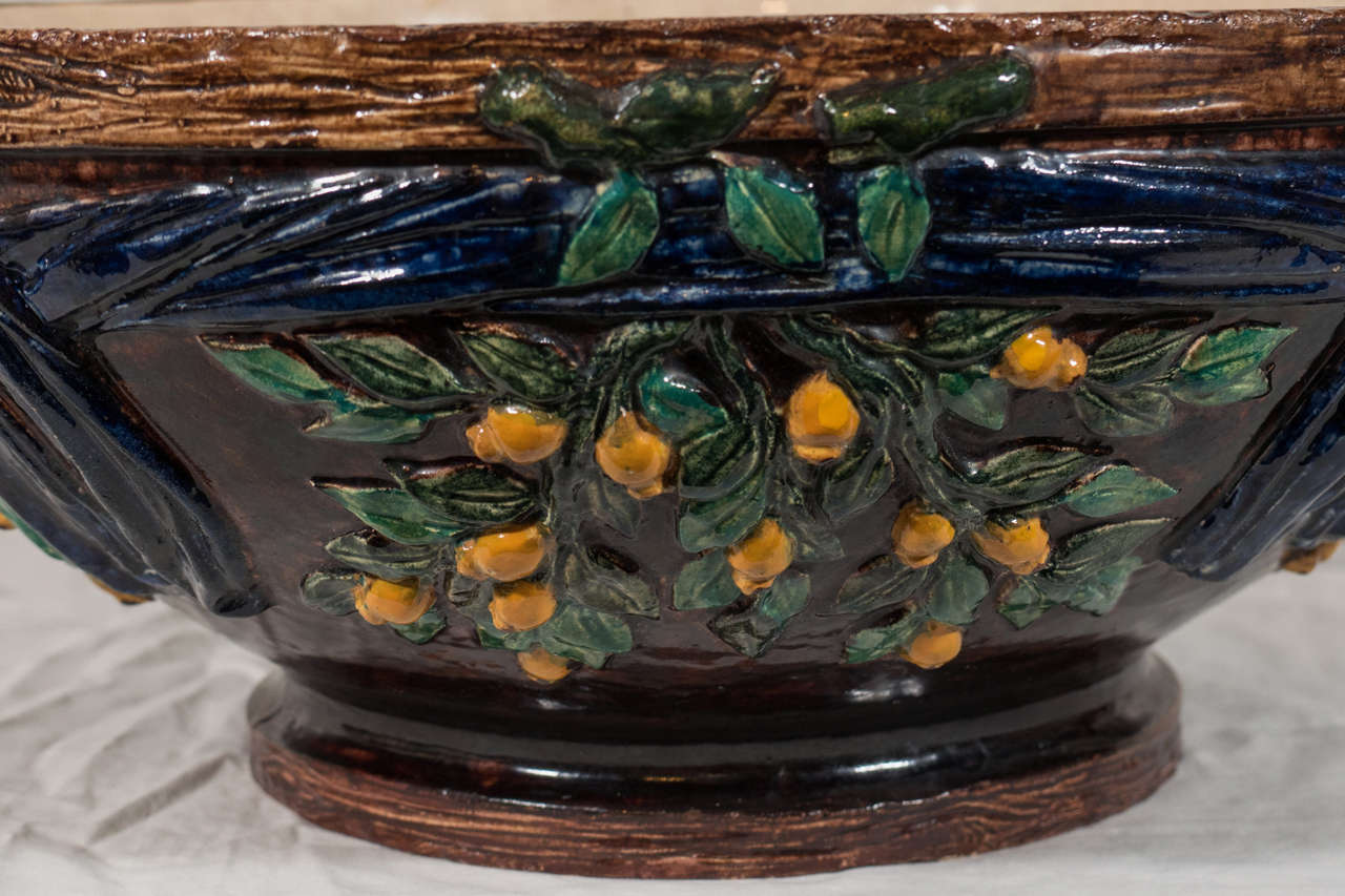 A very large Majolica punch bowl painted deep blue decorated with raised lemons, leaves, ribbons, and a brown faux bois rim. 
 The interior painted a pale beige.