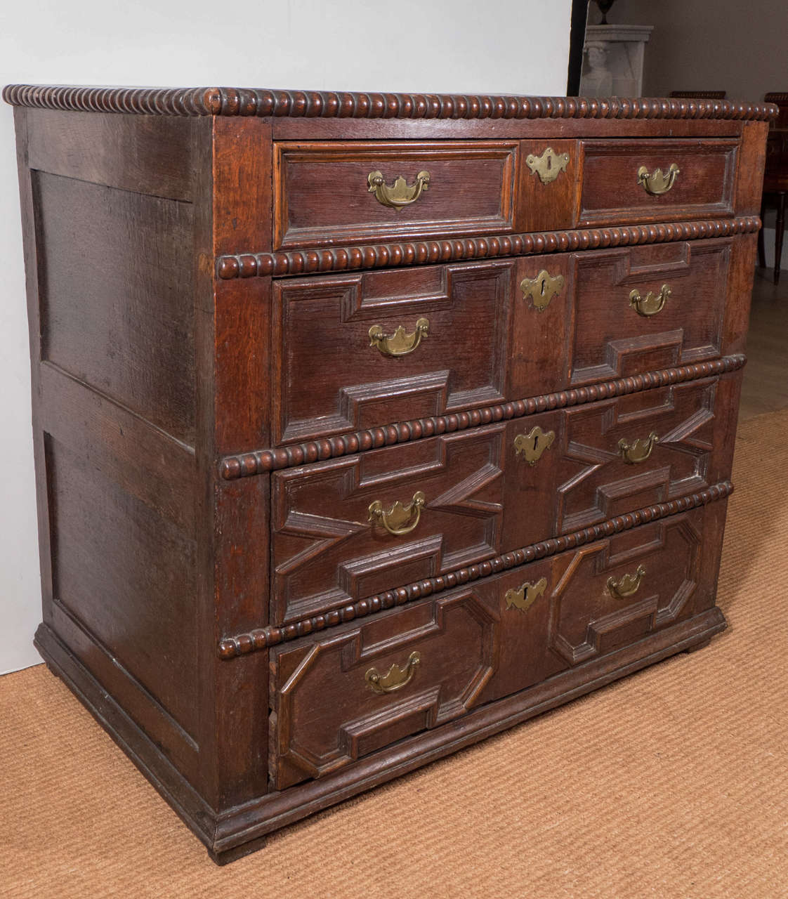 The rectangular top with beaded edge above four geometrically carved drawers, paneled sides, on square block feet, with brass hardware.