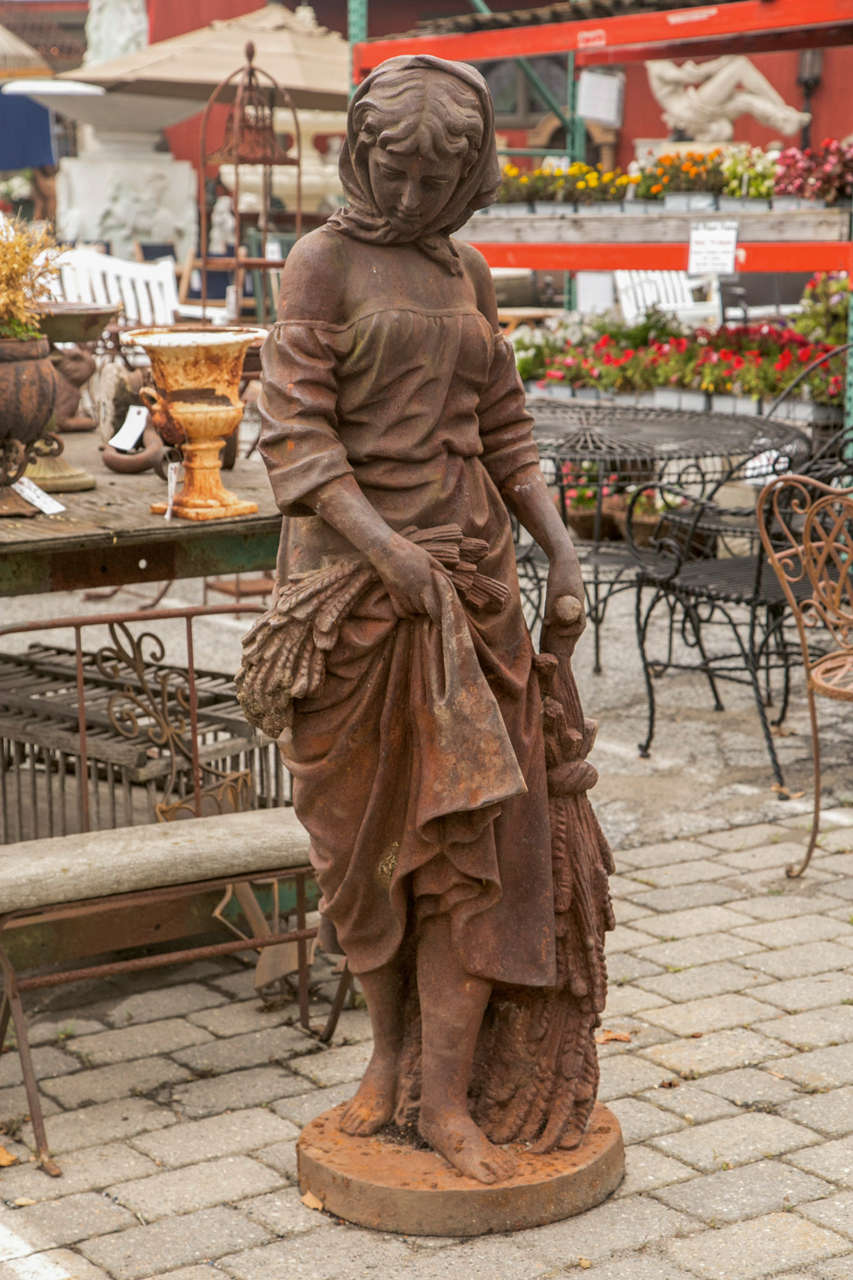 Wonderful, antique iron statue of lady walking back from the fields after a day of work in the fields. She is holding bundles of wheat and barley in both hands. She has a hair bonnet and a handkerchief on her head to keep the sun off of her