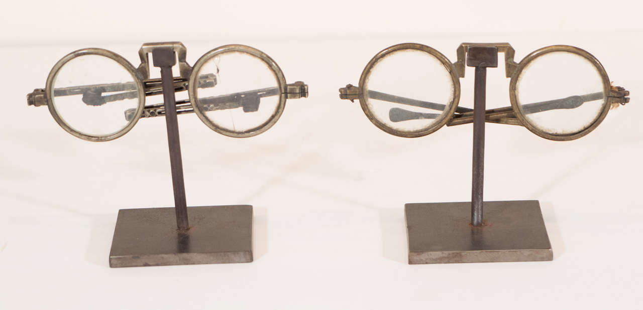 Antique folding eyeglasses on a well crafted custom cast iron stand. Great display objects. Sold individually. One pair of glasses has a single cracked lens. 
From Beijing, circa 1900.  Antique shagreen eyeglass case also available (sold