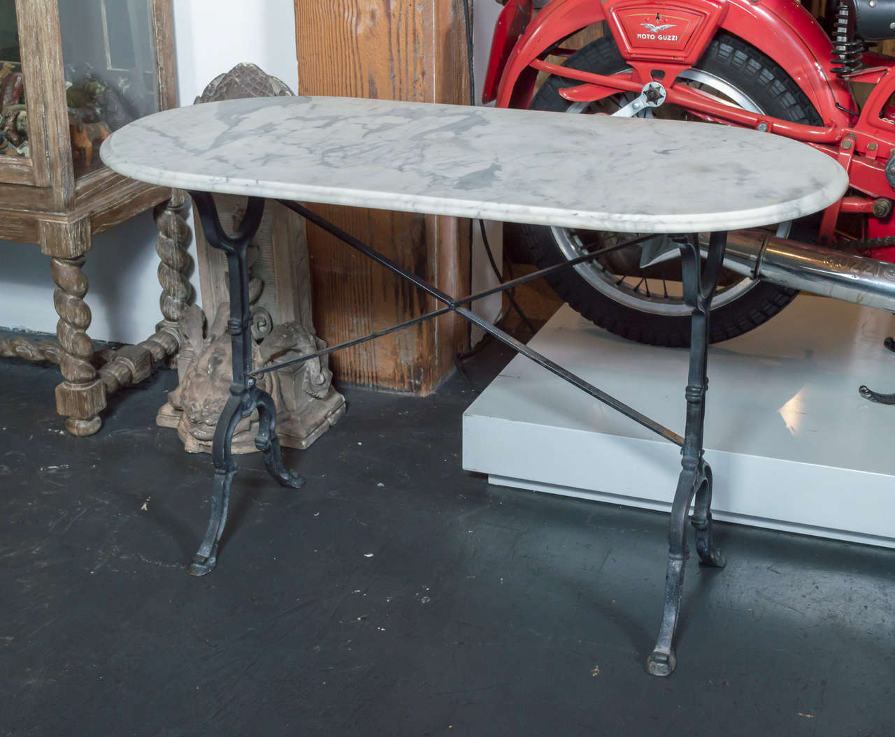 A pair of unique marble garden console tables with iron bases and oval tops. 
The tables are unique in that the iron bases vary slightly in design, and one table is 1.5