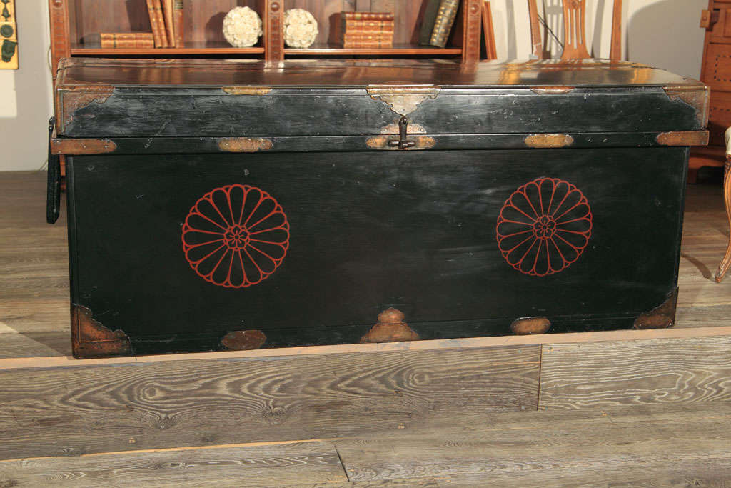 A black lacquer decorative trunk or chest with beautifully embossed brass mounts with red pinwheel decoration to the front and top having oversized handles- interior lined with paper.