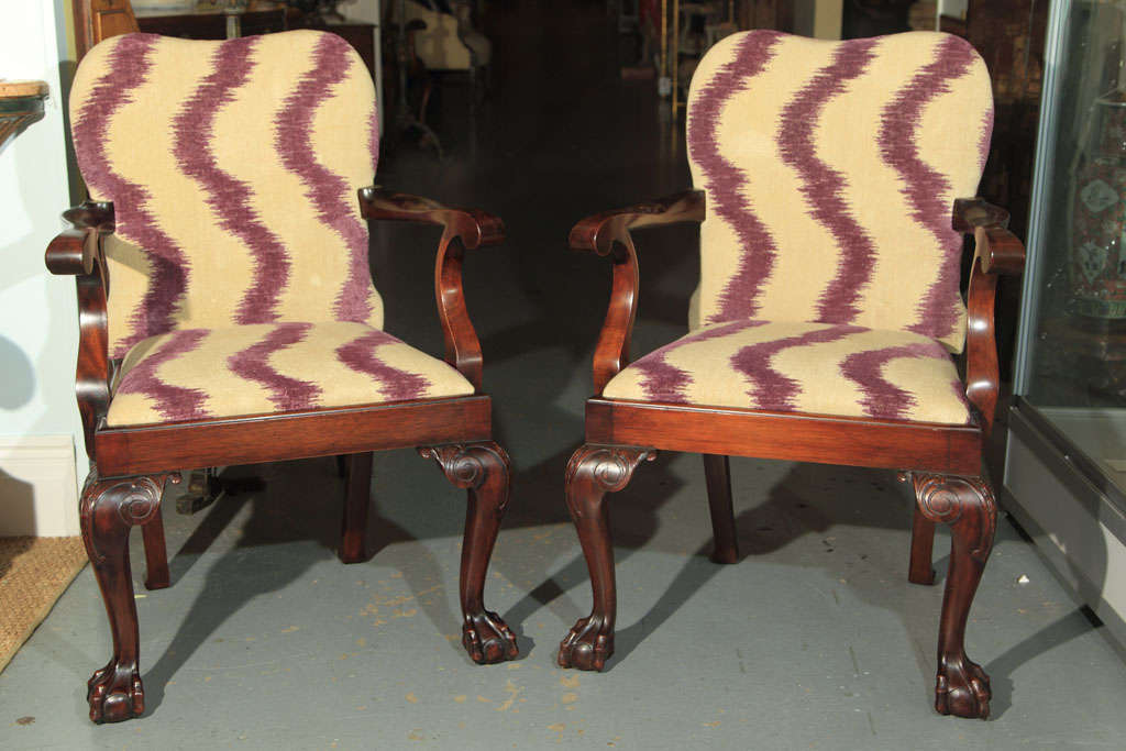 A pair of English bench made, newly upholsted mahogany open armchairs with carved legs ending on ball and claw feet.