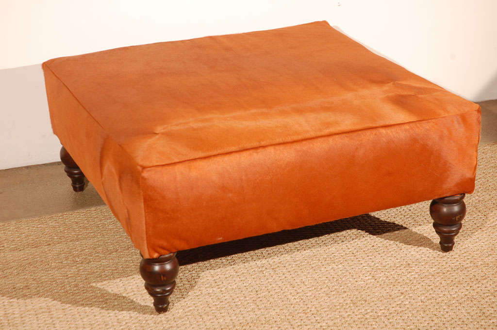 Cozy square ottoman newly reupholstered in a fabulous orange cowhide. Sits elevated on four turned legs, and perfect for use as an ottoman to put your feet up or coffee table with tray in a living room or family room.